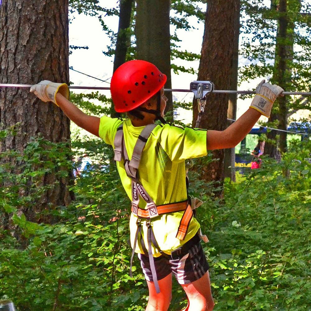 Ein Junge mit rotem Helm und Handschuhen an klettert in einem Kletterwald